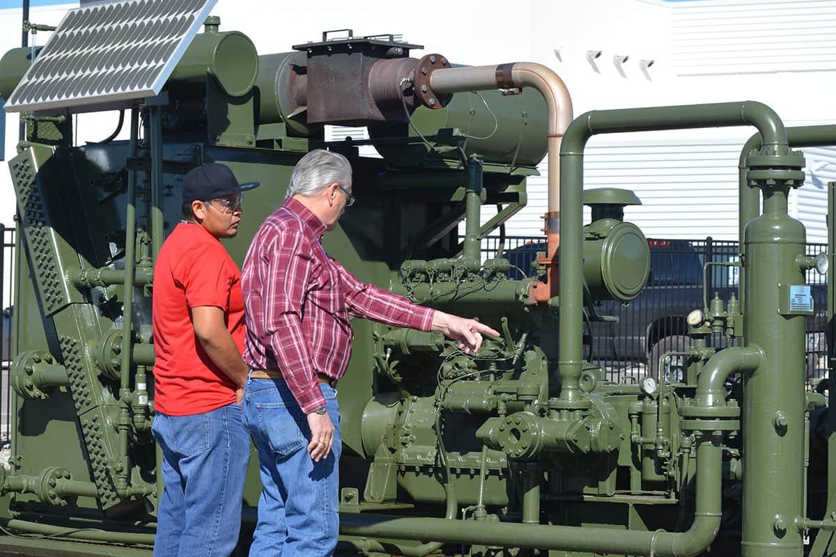 Two individuals look and point at natural gas valves in an outdoor setting